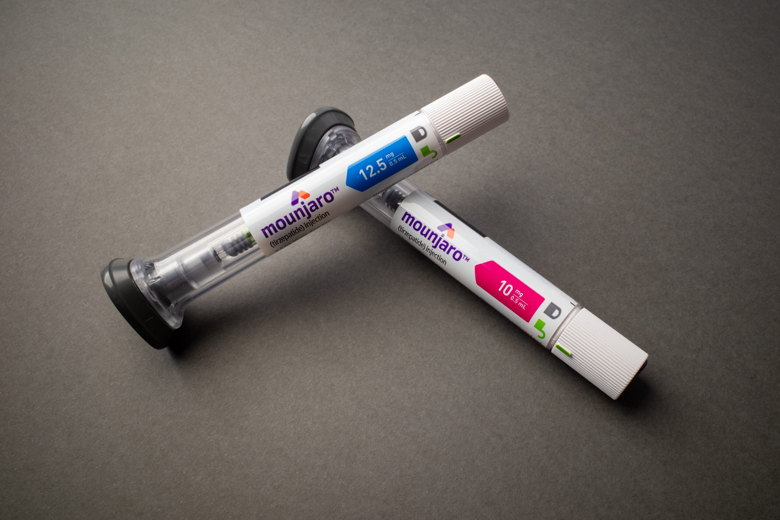 A imagem mostra duas canetas injetoras do medicamento Mounjaro (Tirzepatida) posicionadas uma superfície cinza.